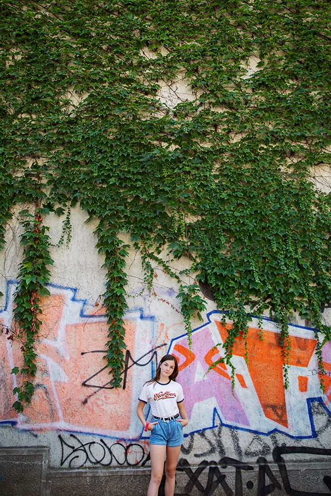 Teen girl in front of a vine covered wall of graffiti in Slovenia