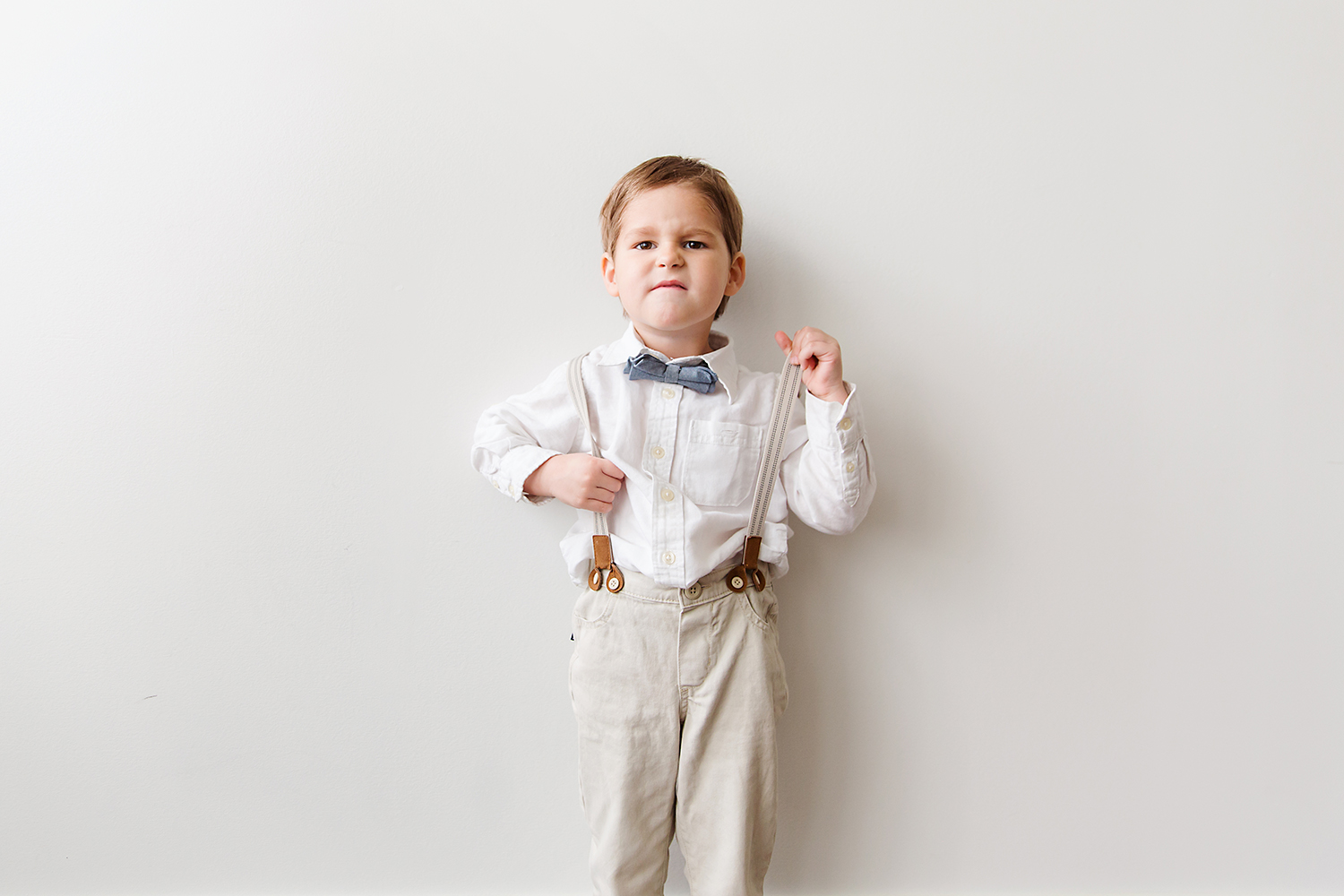 Studio portrait of a grumpy boy in suspenders and a bow tie