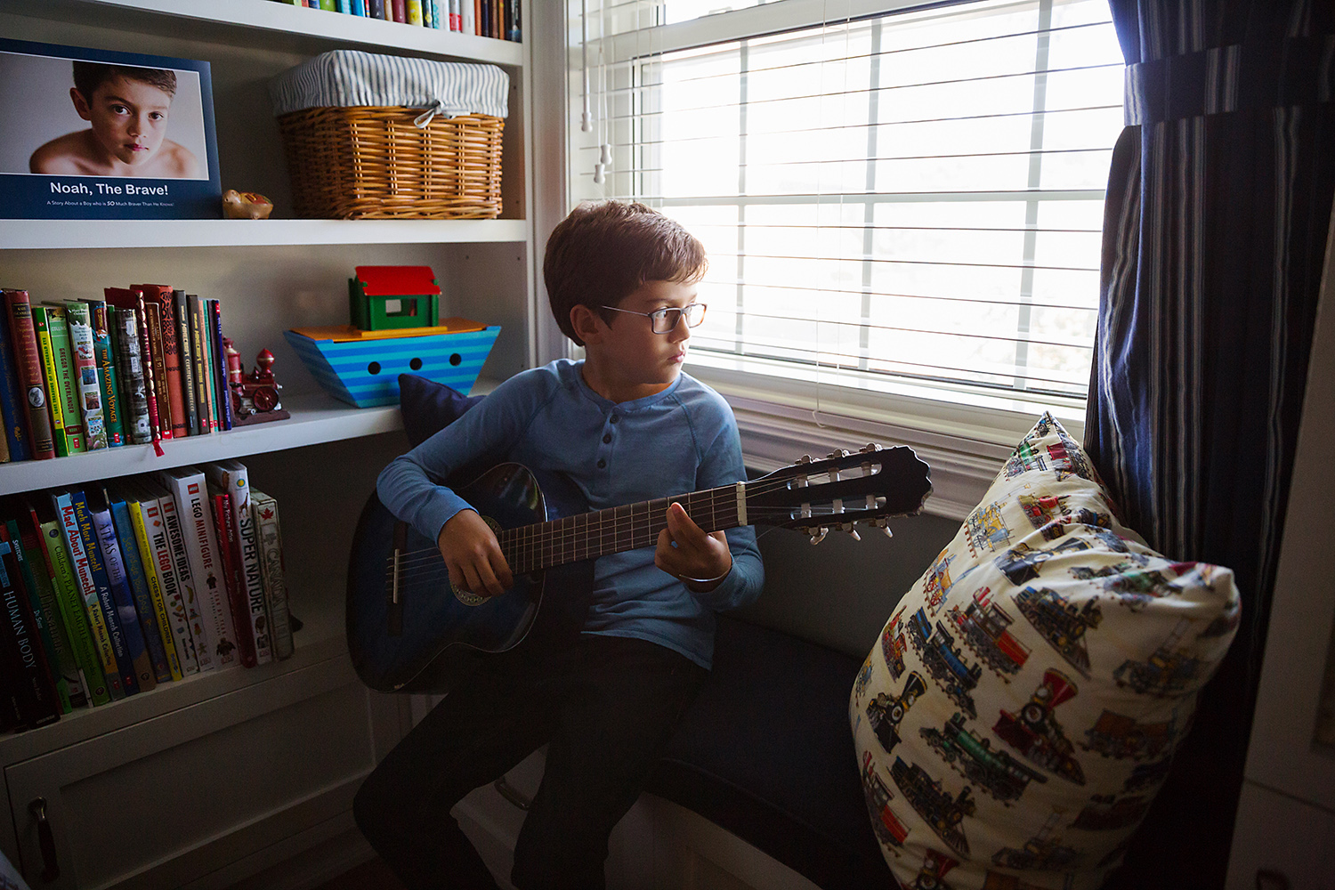 Tween boy playing his guitar on a window seat