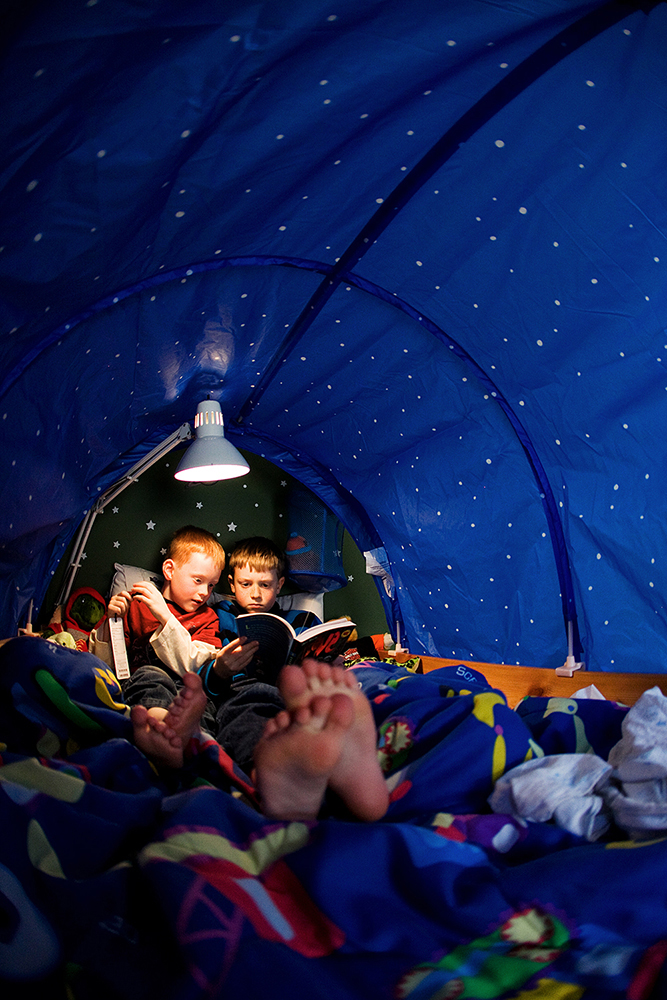Brothers reading books together in a tent