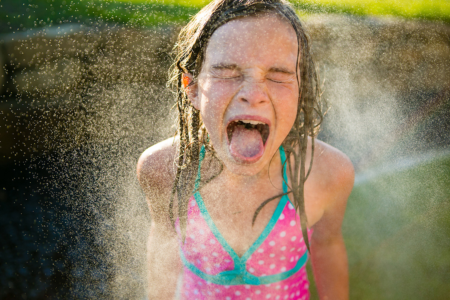 A quirky photograph of a girl playing in a sprinkler by Dana Pugh